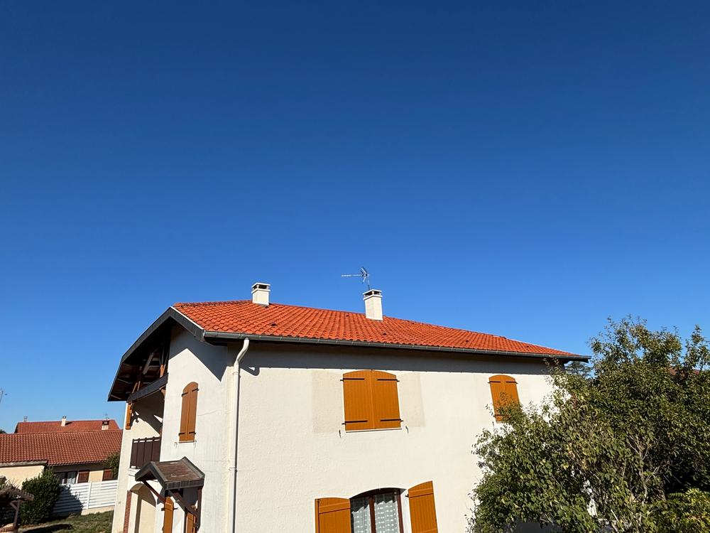 Façade enduite blanche d'une maison aux volets orange, sous un ciel bleu